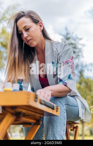 Artista che prepara pentole di vernice su un tavolo mentre si siede di fronte a una tela Foto Stock