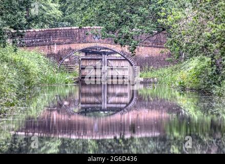 Il ponte di Cowpath vicino a Pirbright si riflette nelle acque ferme dello splendido canale di Basingstoke in Surrey Foto Stock