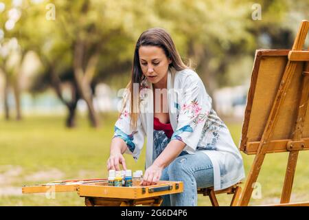Artista che dispone pentole di vernice su un tavolo mentre si siede di fronte a una tela Foto Stock