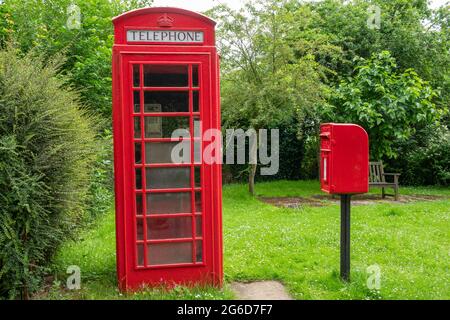 Una scatola telefonica rossa K6 e una scatola di distacco in ghisa montata su palo rosso in un ambiente rurale Foto Stock