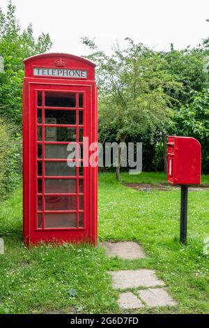 Una scatola telefonica rossa K6 e una scatola di distacco in ghisa montata su palo rosso in un ambiente rurale Foto Stock