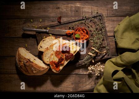 Dall'alto di appetitose fette di pane fresco fatto in casa con pomodori secchi ed erbe aromatiche su rustico tavolo di legno Foto Stock