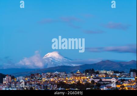 Quito città di notte durante l'ora blu con il vulcano Cayambe, Ecuador. Foto Stock