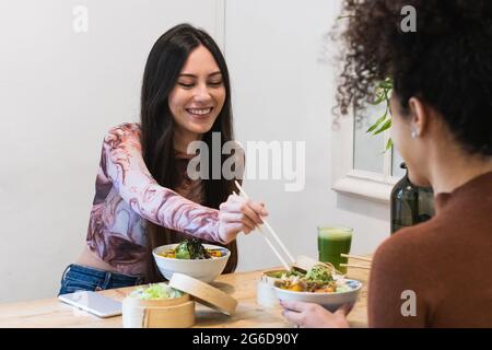 Diverse amiche sedute al tavolo e gustose poke mentre trascorrono il fine settimana al ristorante Foto Stock