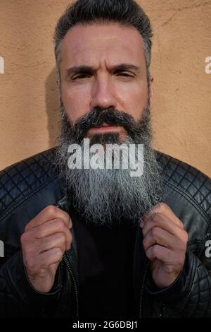 Bel maschio maturo con barba grigia su sfondo marrone in studio guardando la macchina fotografica Foto Stock