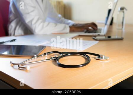 Crop African American femmina medico che scrive rapporto sul computer portatile mentre lavorando al tavolo in un moderno studio clinico Foto Stock