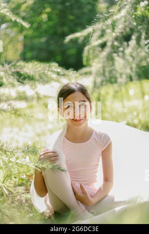 Contenuto ragazza adolescente in abito da ballo e scarpe punta giocando con panno trasparente sul prato in parco il giorno di sole Foto Stock