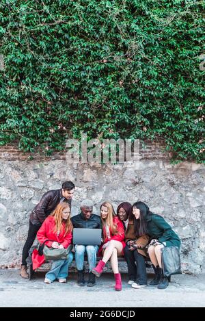 Compagnia di studenti diversi che fanno i compiti insieme mentre si usa netbook in città strada Foto Stock