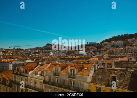 Vista panoramica dello skyline di Lisbona in una giornata estiva soleggiata con i tradizionali tetti arancioni del quartiere di Alfama con il mare visibile nel paesaggio Foto Stock