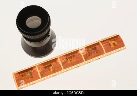 Striscia di pellicola negativa a colori da 35 mm e lente di ingrandimento sul piano luminoso Foto Stock
