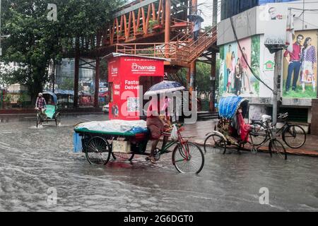 Dhaka, Bangladesh. 04 luglio 2021. Un ciclista ripara dalla pioggia sotto un ombrello durante una pioggia. Il paese è entrato in un blocco rigoroso e pesante monsone downpour ha causato il disboscamento estremo di acqua nella maggior parte delle zone della città di Dhaka, il Bangladesh. Le strade sono state sommerse rendendo la marcia lenta e pericolosa. Credit: SOPA Images Limited/Alamy Live News Foto Stock