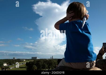 Un bambino si siede sulle spalle dei suoi padri, coprendo le orecchie e stringendo un razzo modello, mentre si prepara per il liftoff del razzo Delta IV GPS III Magellan di United Launch Alliance il 22 agosto 2019, alla stazione dell'aeronautica di Cape Canaveral, Fla. Il GPS-III, visto in lontananza, Lanciato da Space Launch Complex-37, rappresenta il passo successivo nella modernizzazione della rete di navigazione a livello mondiale con una nuova generazione di satelliti per offrire maggiore precisione, migliore resilienza e un nuovo segnale per gli utenti civili. (STATI UNITI Air Force foto di Airman prima Classe Zoe Thacker) Foto Stock