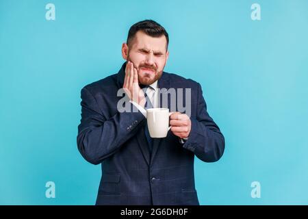 Mal di denti. Ritratto di uomo arrabbiato in abito elegante che soffre di terribile dolore ai denti dopo aver bevuto bevande calde o fredde, lesioni dentali. Interno Foto Stock