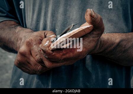 Primo piano delle mani dell'uomo che tengono un coltello e un pezzo di legno, vista orizzontale, sul paesaggio Foto Stock
