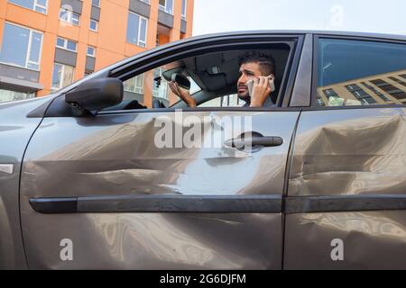 Ritratto di triste bell'uomo sopportato seduto in auto ammaccata e parlare telefono cellulare, chiamando a ispezione di assicurazione o chiedendo a qualcuno di aiutare, strada AC Foto Stock