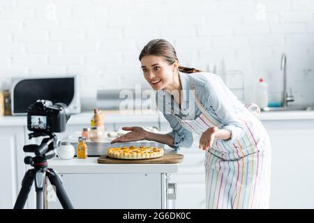 buon blogger culinario che punta con le mani a torta deliziosa vicino sfocato fotocamera digitale Foto Stock