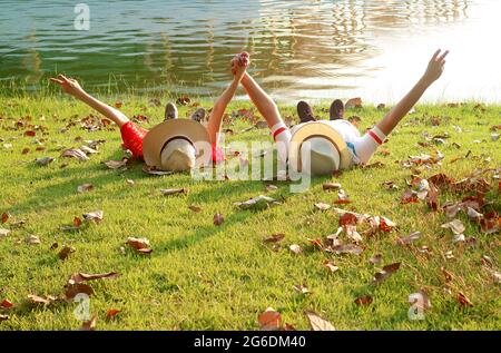 Felice coppia in cappello di paglia che si stese insieme alzando le braccia con il segno V sul lago Foto Stock