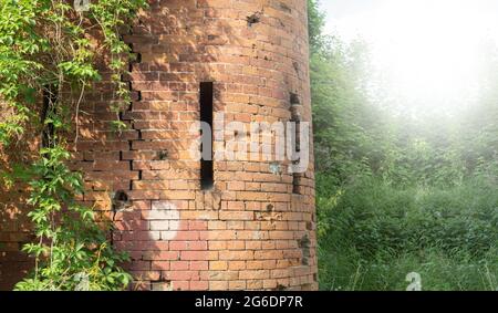 Un'antica torre medievale con scappatoie per le armi. Frammento di una torre con scappatoie nel muro di pietra rossa. Spazio di copia Foto Stock