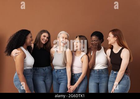 Eleganti donne di diverse età che si divertono mentre indossano jeans e magliette su sfondo marrone Foto Stock
