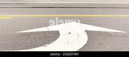 Grande freccia bianca di direzione verniciata sulla strada segnalando una svolta a sinistra Foto Stock