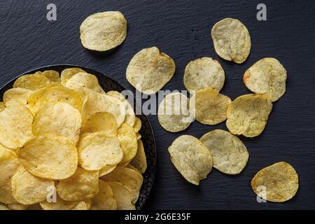 Vista dall'alto su una patata croccante su una piastra in ceramica nera su una superficie nera. Gustoso spuntino di sottili fette di patate fritte. Pronto a mangiare fastfood. Foto Stock