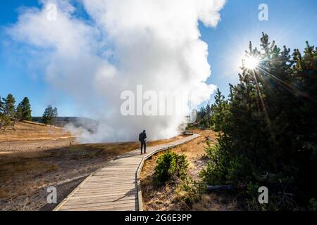 Camminate sul ponte pedonale vicino alle sorgenti termali calde fumanti, al sole con la stella del sole, al Churning Caldron, al Yellowstone National Park, Wyoming, USA Foto Stock