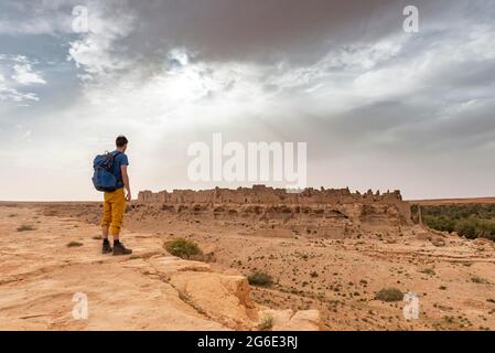 Giovane uomo a bordo di una scogliera, nelle rovine posteriori della città vecchia presso l'oasi Source Bleu, Blue Spring, Madkhal Meski, Marocco Foto Stock