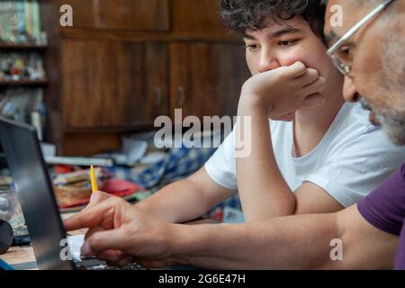 Nonno sta insegnando una lezione a suo nipote sul monitor del laptop a casa Foto Stock