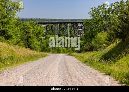 Una strada in ghiaia che conduce ad un ponte ferroviario alto traliccio. Foto Stock