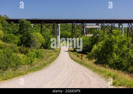 Una strada in ghiaia che conduce ad un ponte ferroviario alto traliccio. Foto Stock