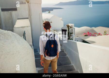 L'uomo che viaggia a Santorini cammina lungo la strada stretta a Fira, Grecia, godendo di vista mare e architettura tradizionale. Turismo, vacanze estive Foto Stock