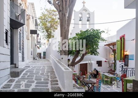 Cafe taverna ristorante vicino alla chiesa di Chora iOS, Nios isola, Cicladi, Grecia. Tavoli colorati tradizionali sedie su strada acciottolata sotto la risata Foto Stock