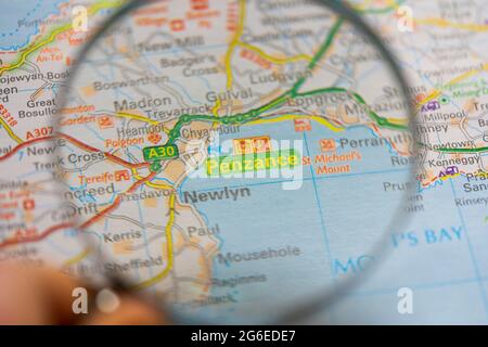 Primo piano di una pagina in un atlante di carta stradale stampata con una mano dell'uomo che tiene una lente di ingrandimento che mostra un ingrandimento di Penzance in Cornovaglia, Inghilterra Foto Stock