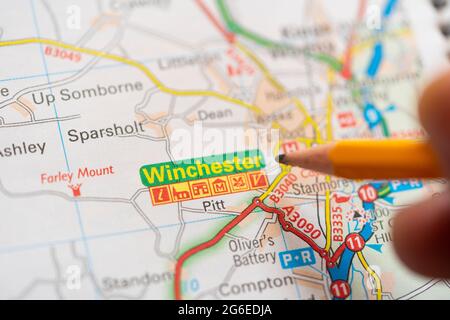 Primo piano di una pagina in un atlante di carta stradale stampata con una mano dell'uomo che tiene una matita che punta alla città di Winchester in Inghilterra. Concetto: Lettura della mappa Foto Stock
