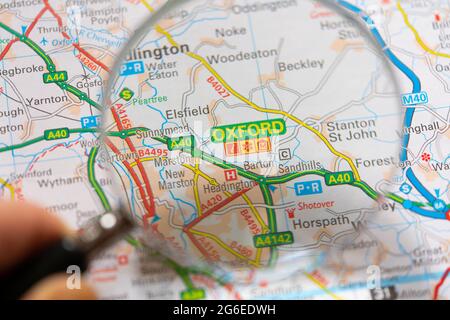 Un closeup macro di una pagina in un atlante della carta stradale stampata con una mano dell'uomo che tiene una lente di ingrandimento che mostra un ingrandimento di Oxford in Inghilterra Foto Stock