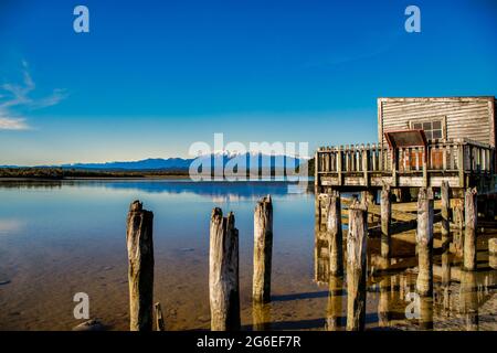 La storica Boathouse in legno sulla riva del lago Okarito con le alpi meridionali sullo sfondo Foto Stock