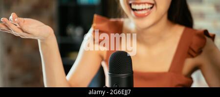Primo piano di una giovane bella donna che sorride seduto sulla scrivania utilizzando un laptop e un podcast di registrazione microfono durante l'intervista Foto Stock