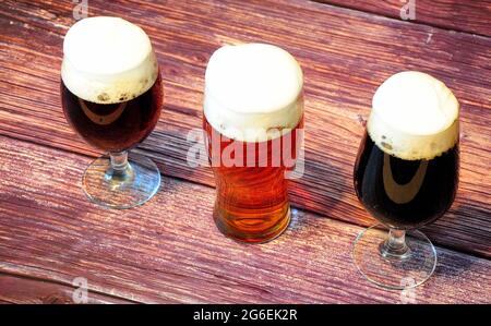 Tre diversi bicchieri, con diversi tipi di birra scura, si trovano in fila su un tavolo di legno. Vista laterale. Foto Stock