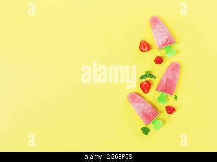 Piatto con gelato al sorbetto congelato rosa fruttato su bastone di plastica verde con tagli di fragola, foglie di menta su sfondo giallo. Congelato Foto Stock