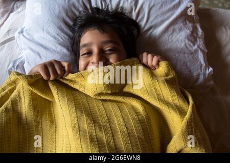 Vista dall'alto di un ragazzo a letto che si sveglia con l'uso della messa a fuoco selettiva. Concetto di una domenica pigra a letto. Foto Stock