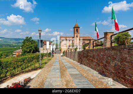 Stretta passerella in ciottoli lungo le mura in mattoni come piccola chiesa parrocchiale sotto il bel cielo sullo sfondo nella città di Grinzane Cavour in Piemonte, Italia. Foto Stock