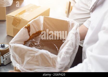Confezionamento di cioccolata calda e pasta di cioccolato nella produzione di dolciumi. Preparazione di crema di latte condensato e crema per torte Foto Stock