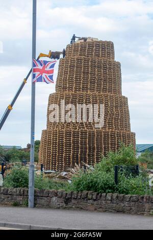 4 luglio 2021 giovani in cima al falò molto alto fatto da migliaia di pallet industriali in legno in preparazione per le celebrazioni del 12 luglio Foto Stock