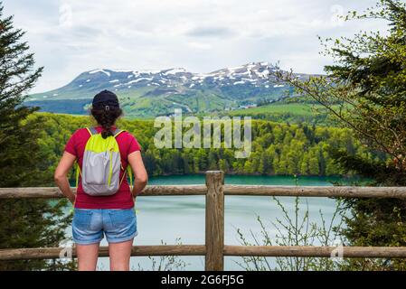 Giovane donna (irriconoscibile vista posteriore) ammirando la vista del lago Pavin nel Parco Naturale Regionale dei Vulcani d'Alvernia, Francia. Vacanze attive in natura backg Foto Stock