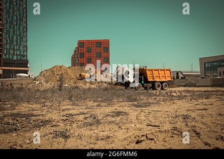 Escavatore da costruzione giallo e un grande dumper in un cantiere con mucchi di sabbia sullo sfondo di nuovi edifici alti Foto Stock