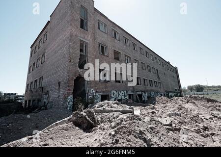 Edificio in mattoni demolito con finestre di vetro rotte che si ergono da sole in un campo con detriti. Un'immagine a toni Foto Stock