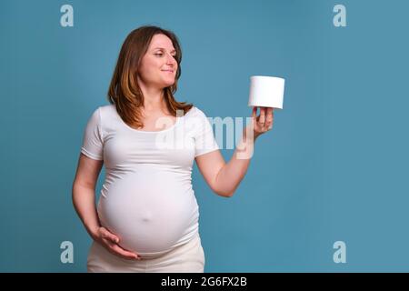 Carta igienica in mani di donna incinta, studio girato su sfondo blu Foto Stock