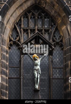 Statua di Gesù sul crocifisso appeso di fronte alla vecchia chiesa abbandonata. Color oro davanti alla finestra in vetro colorato. Foto Stock