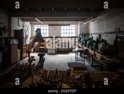 Abbandonata vecchia officina sporco camera polverosa e deserta. L'industria e gli attrezzi si siedono inutilizzati, moody atmosfera creepy luce naturale inquietante. Maestria artigianale Foto Stock