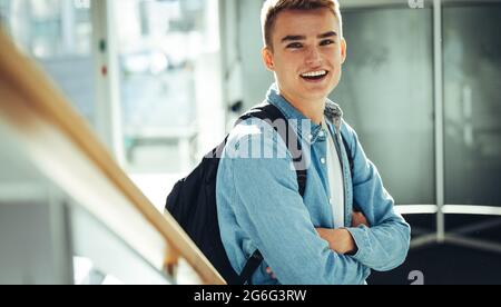 Giovane uomo nel campus universitario in piedi con le braccia incrociate sorridendo alla macchina fotografica. Felice studente di sesso maschile in università. Foto Stock